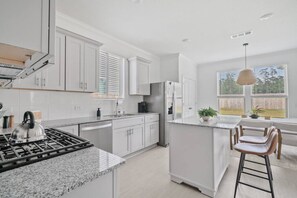 Una cocina moderna con armarios blancos, encimera de granito, refrigerador de acero inoxidable y estufa a gas.