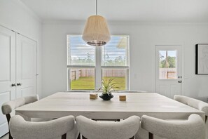 Un comedor con una mesa grande, seis sillas, una lámpara colgante y vista a un jardín trasero a través de una ventana.