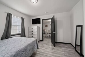 A bedroom with a bed, a dresser, a TV, and a door leading to a dining area. - Cozy 3-Bedroom Suburban Retreat near Downtown (Houston)