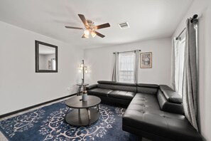 A modern living room with a sectional sofa, a round coffee table, a floor lamp, and a ceiling fan. - Cozy 3-Bedroom Suburban Retreat near Downtown (Houston)