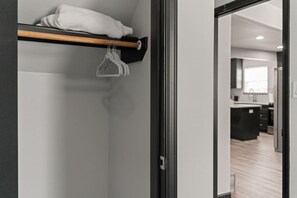 Een modern interieur met een houten plank waarop een witte handdoek en een kleerhanger liggen. Een deur leidt naar een keuken met een houten vloer.