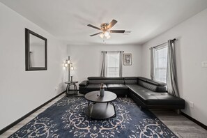 A modern living room with a sectional sofa, a round coffee table, a ceiling fan, and a patterned rug. - Cozy 3-Bedroom Suburban Retreat near Downtown (Houston)