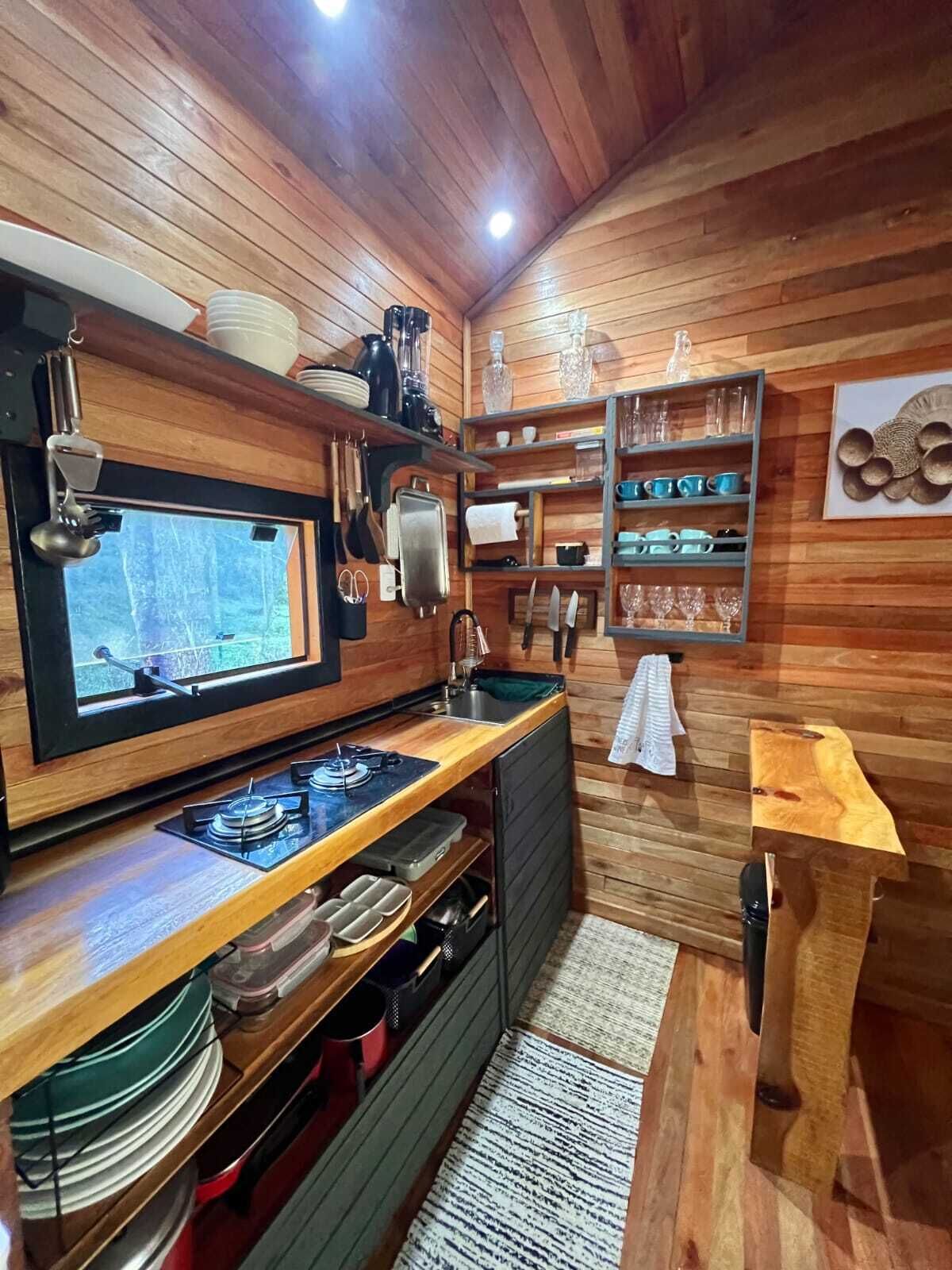 A compact kitchen with wooden walls, a built-in stove, and shelves with dishes and glasses.