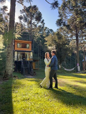 A couple dancing in a grassy area with a wooden cabin and a hammock in the background. - Frost Cabin • Urubici, SC | Private Stream, your retreat with a hot tub. (Urubici)