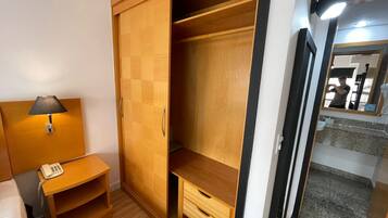 Quarto com guarda-roupa de madeira, mesa de cabeceira com abajur e espelho.