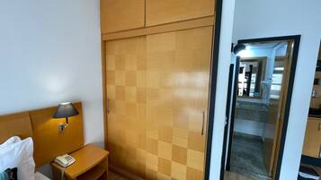 Quarto de hotel com cama, mesa de cabeceira, abajur e guarda-roupa xadrez.