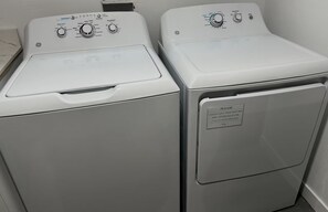 Dos lavadoras blancas de carga frontal apiladas, con paneles de control y una etiqueta de advertencia de seguridad.