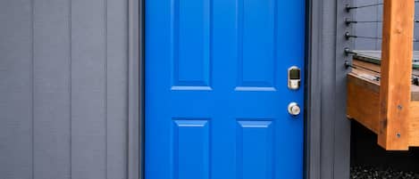 Une porte bleue avec un paillasson sur lequel est écrit « Bienvenue », une boîte aux lettres et une structure en bois portant la lettre « B ».