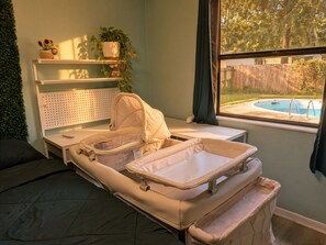 Una habitación con cama, mesita de noche, ventana con vista a una piscina y estante con plantas.