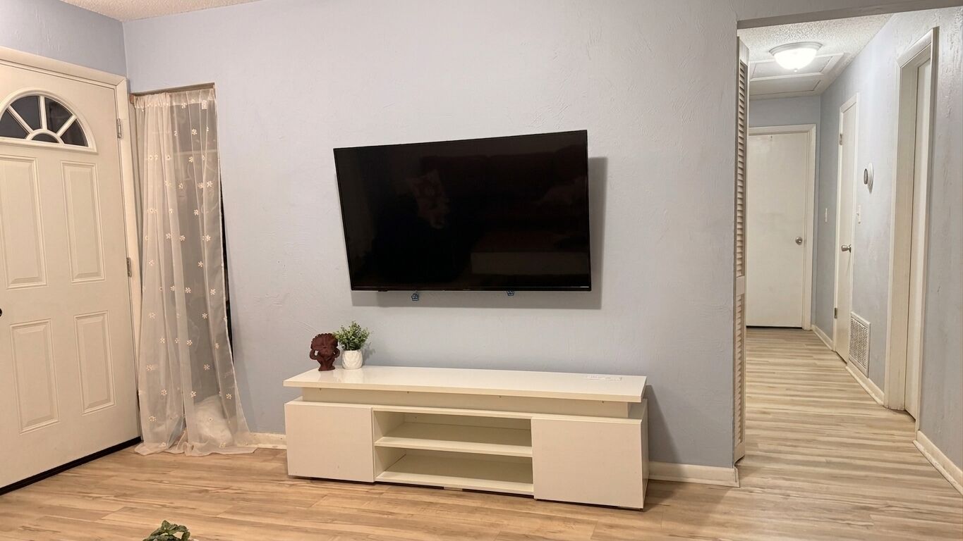 A room with a mounted television on the wall, a white entertainment unit below, and a door with a decorative curtain.