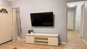A room with a mounted television on the wall, a white entertainment unit below, a door with a decorative glass panel, and a hallway leading to another room.