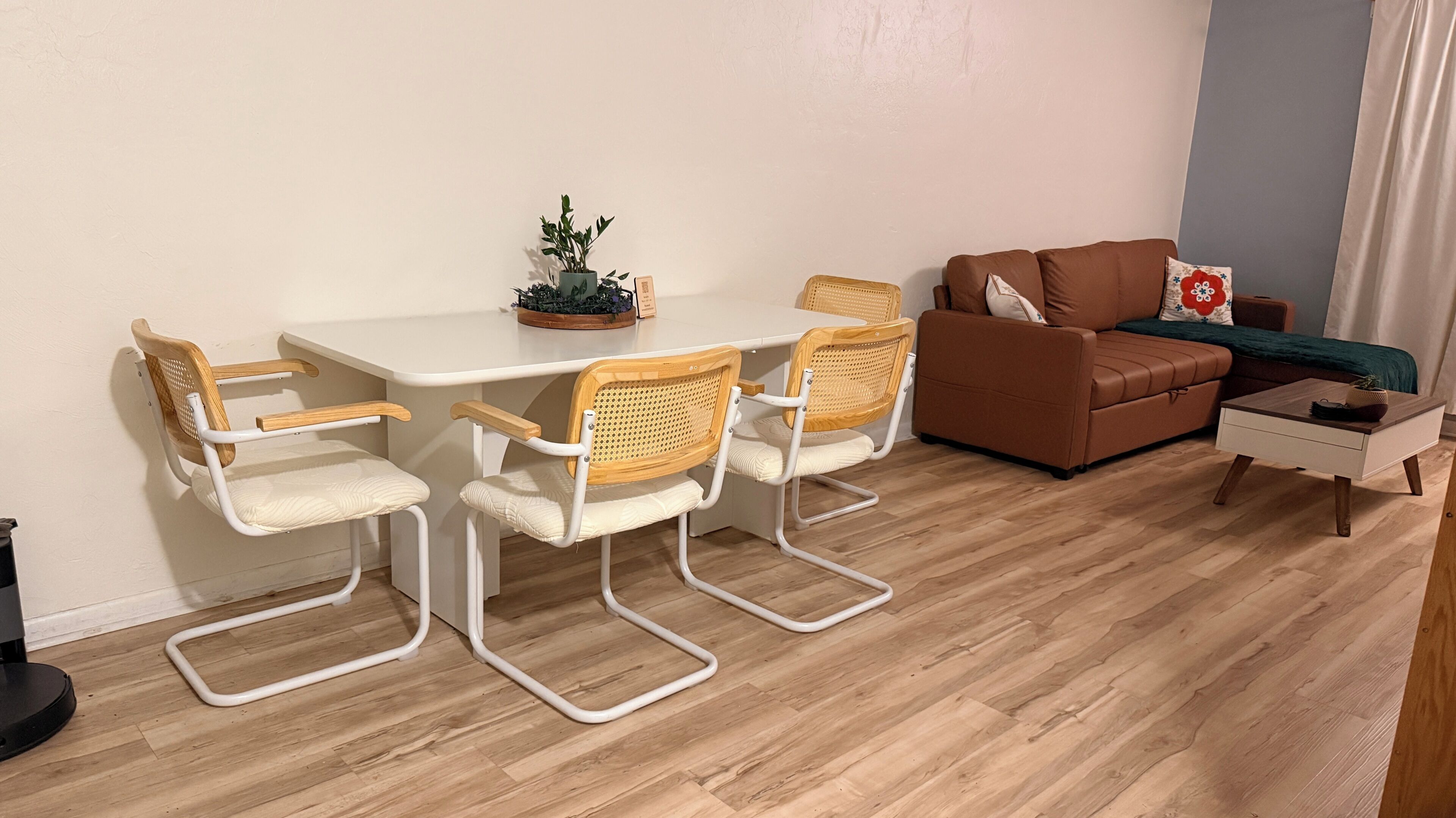 Ein Wohnzimmer mit einem weißen Tisch, vier Stühlen, einem braunen Sofa und einem kleinen Beistelltisch.