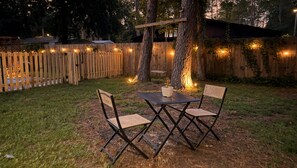 Un área de estar al aire libre con una mesa y sillas, rodeada por una valla de madera y luces colgantes.