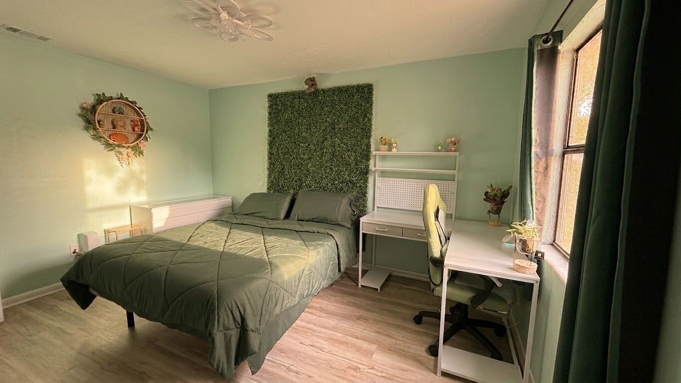 A bedroom with a bed, desk, chair, and a wall-mounted shelf.