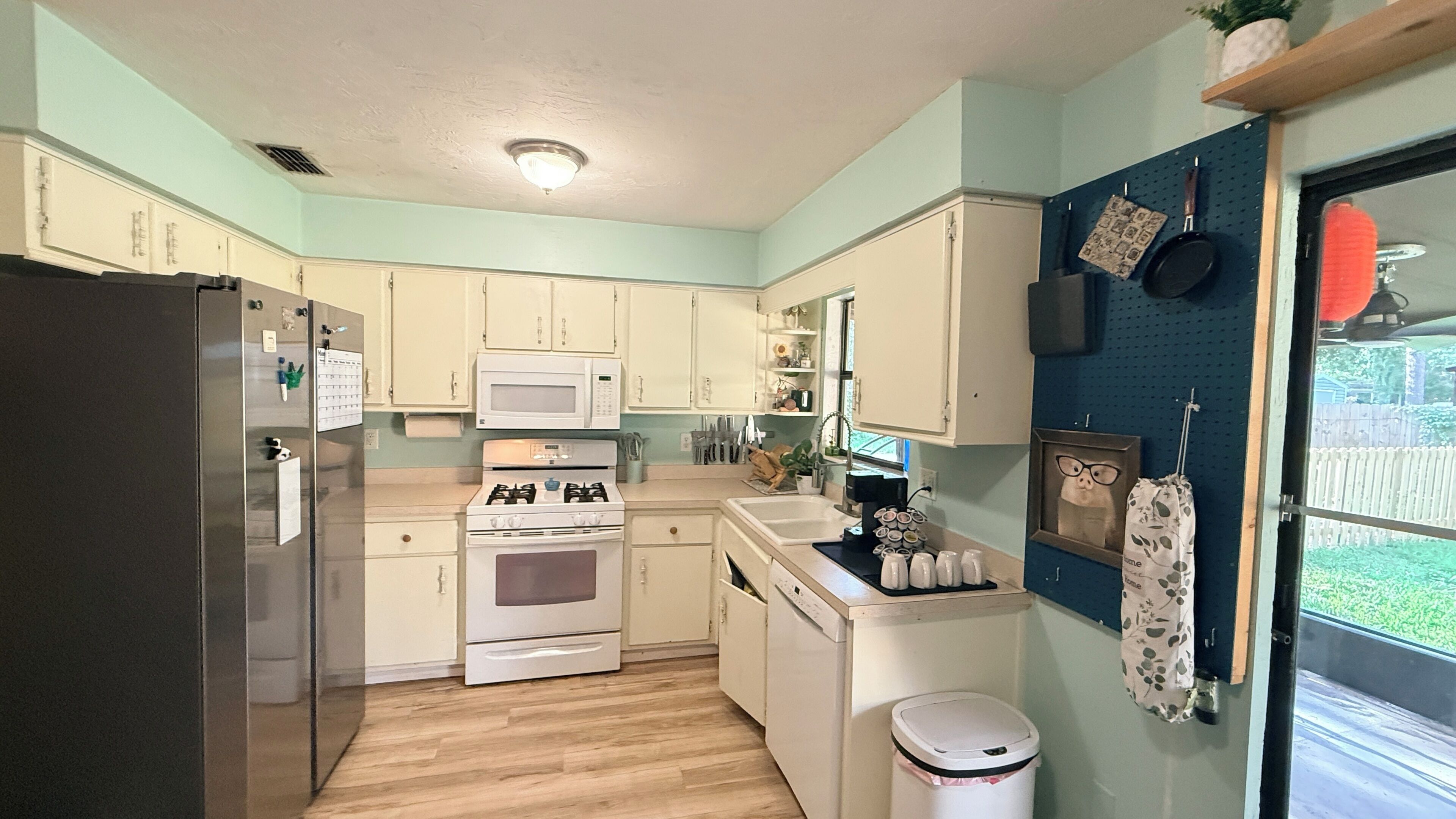 A compact kitchen with white cabinets, a stainless steel refrigerator, a microwave, an oven, and a sink.