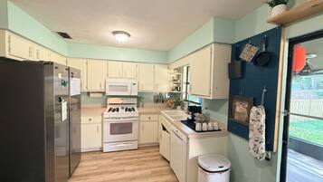 A compact kitchen with white cabinets, a stainless steel refrigerator, a microwave, an oven, and a sink.