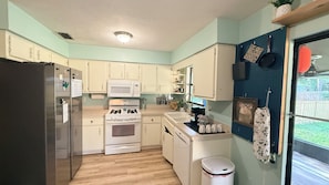 A compact kitchen with white cabinets, a stainless steel refrigerator, a microwave, an oven, and a sink.
