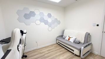 A room with a grey sofa, a white chair, and a wall-mounted hexagonal light fixture.