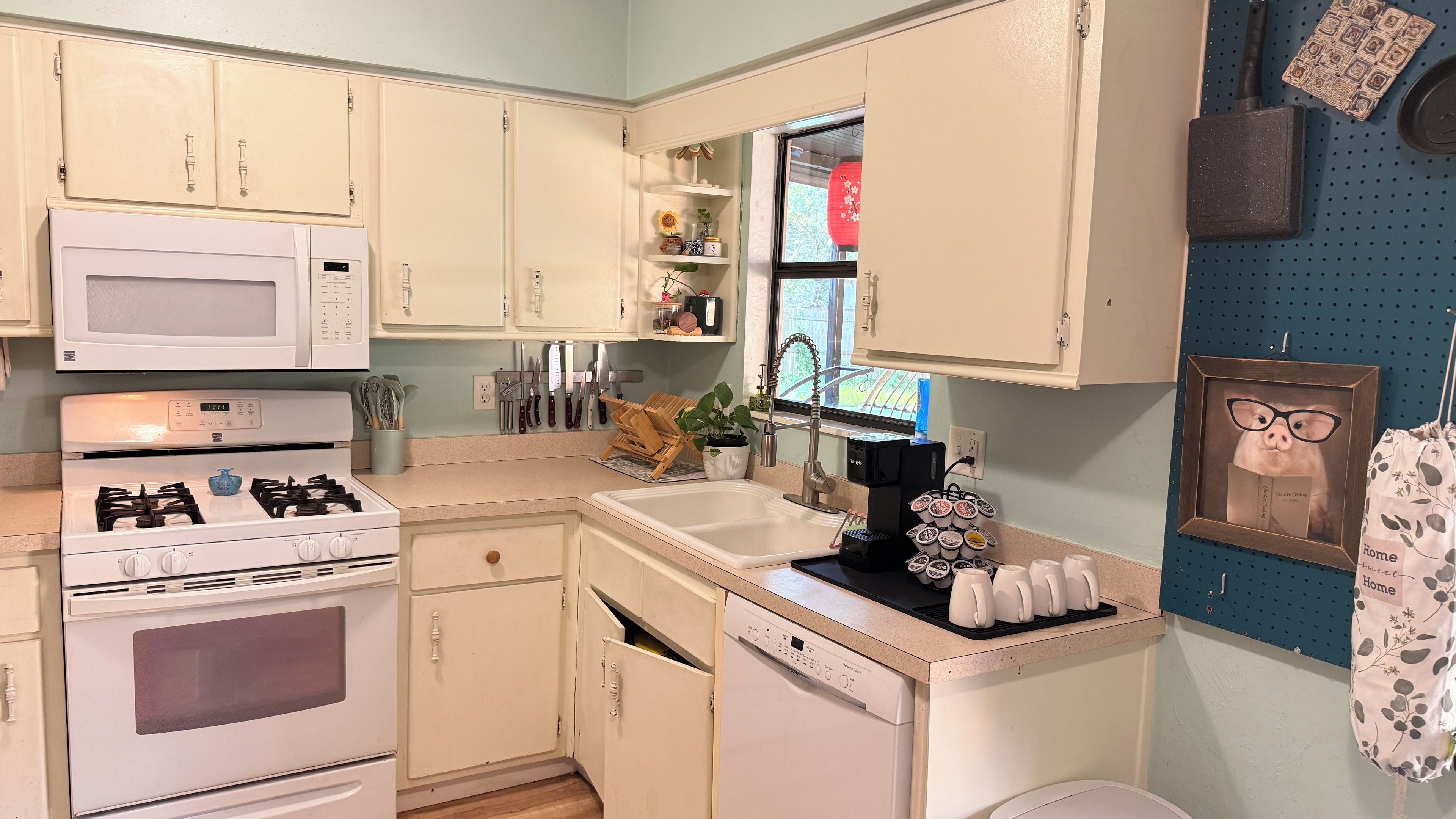 A compact kitchen with white appliances, a sink, and a window with a view.