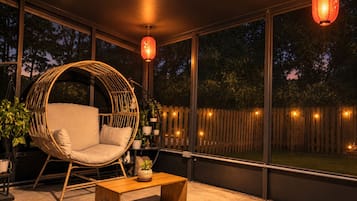 A cozy outdoor seating area with a wicker chair, a wooden table, and potted plants.