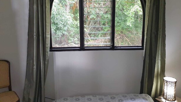 Ein Zimmer mit einem Bett, einem Sessel, einem Fenster mit Blick auf Grünflächen und einer Lampe auf einem Nachttisch.