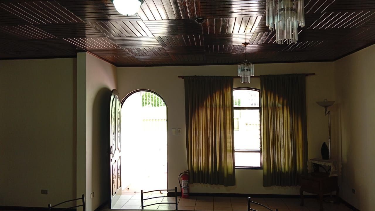 A room with a wooden ceiling, a large arched window, and a table with chairs.