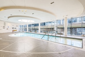 An indoor swimming pool with clear glass walls, a tiled floor, and a modern ceiling design. - Luxury 3 bedrm 2 Baths Steps from CN Tower/Rogers Centers with One Parking Spot (Toronto)