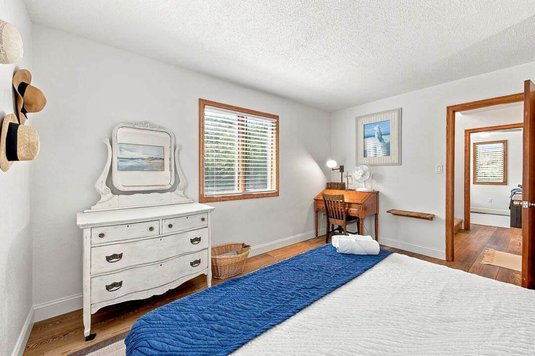 A bedroom with a bed, a desk, a chair, a dresser, and a window with blinds.