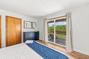 A bedroom with a bed, a dresser, a mirror, and a sliding glass door leading to an outdoor deck. - Salted Skyline | Private Community Beach Access | Hot Tub and Dog Friendly (Kitty Hawk)