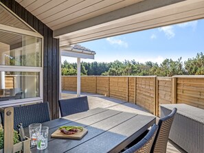 Een terras buiten met een tafel, stoelen, een houten omheining en uitzicht op bomen.