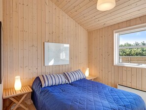 Een kamer met houten wanden, een bed met blauw beddengoed, twee nachtkastjes met lampen en een raam met uitzicht op groen.