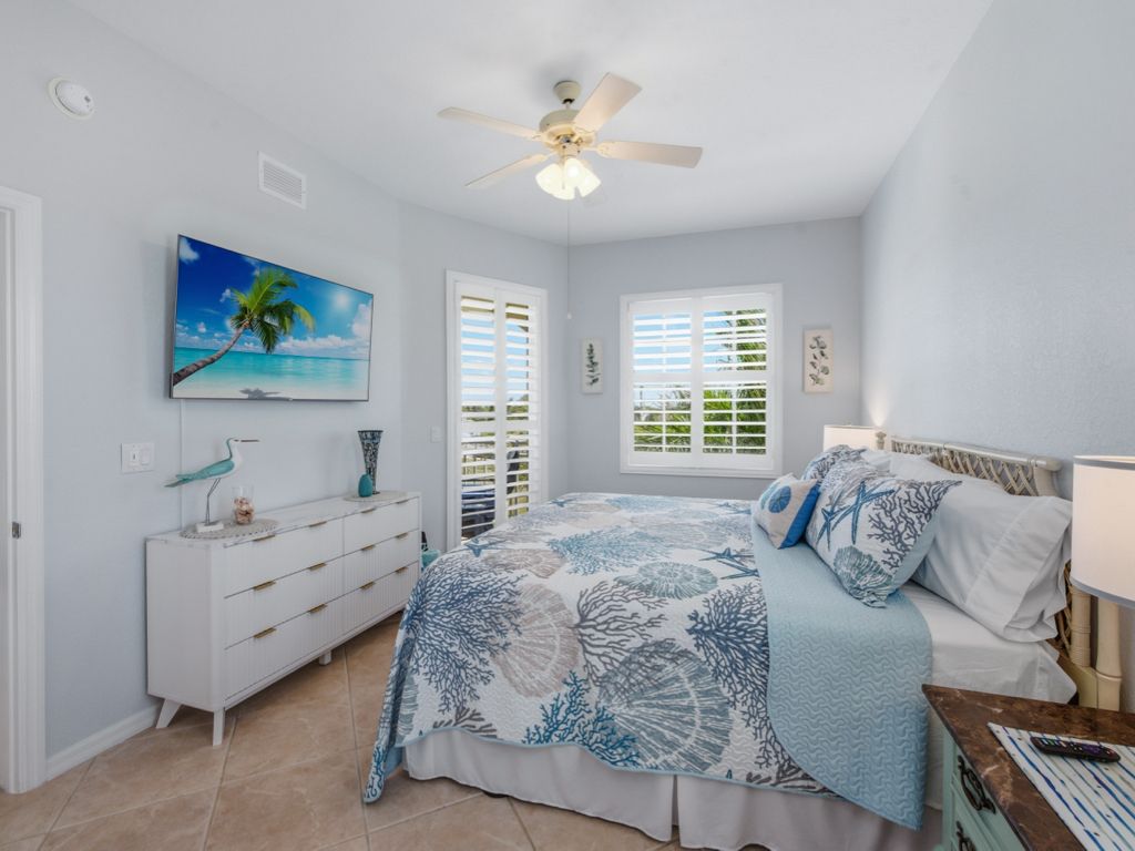 A bedroom with a bed, a dresser, a ceiling fan, and a window with shutters.