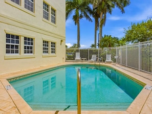 A swimming pool with a clear blue water, surrounded by a white fence, and palm trees in the background. - Marco Island 2 king bed unit + pool with park views. Walk to shops & dining. (Marco Island)