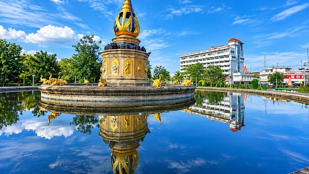 A fountain with a golden spire and statues, surrounded by a reflective pool, with a building in the background.