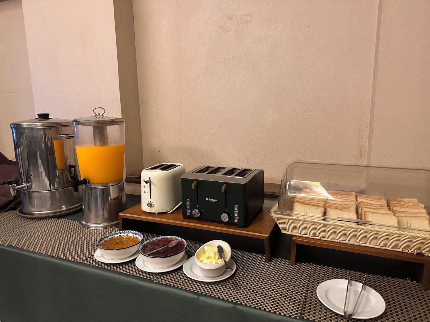 A breakfast buffet setup with a coffee maker, two toasters, and a bread display.