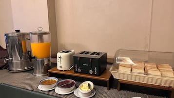 A breakfast buffet setup with a coffee maker, two toasters, and a bread display.