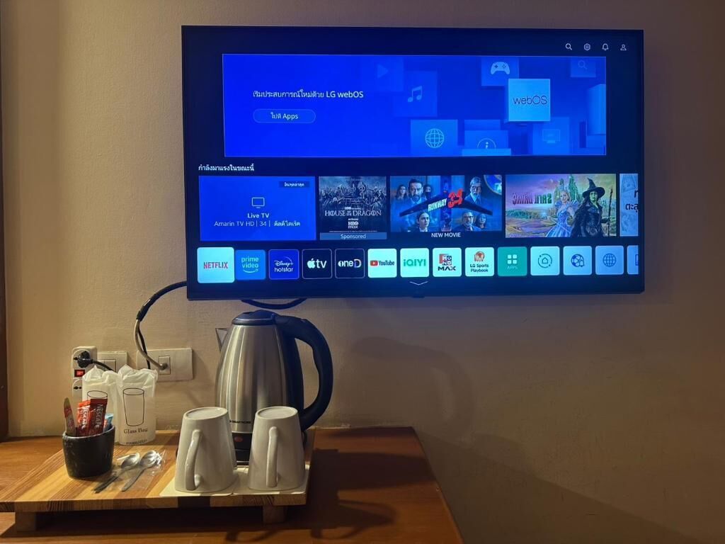 A television mounted on a wall displaying a webOS interface with various app icons and a coffee station below.