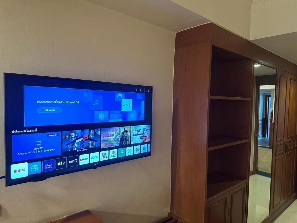 A flat-screen TV mounted on a wall displaying a user interface with various app icons and a live TV channel.