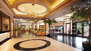 A hotel lobby with a central circular marble area, a chandelier, and potted plants.