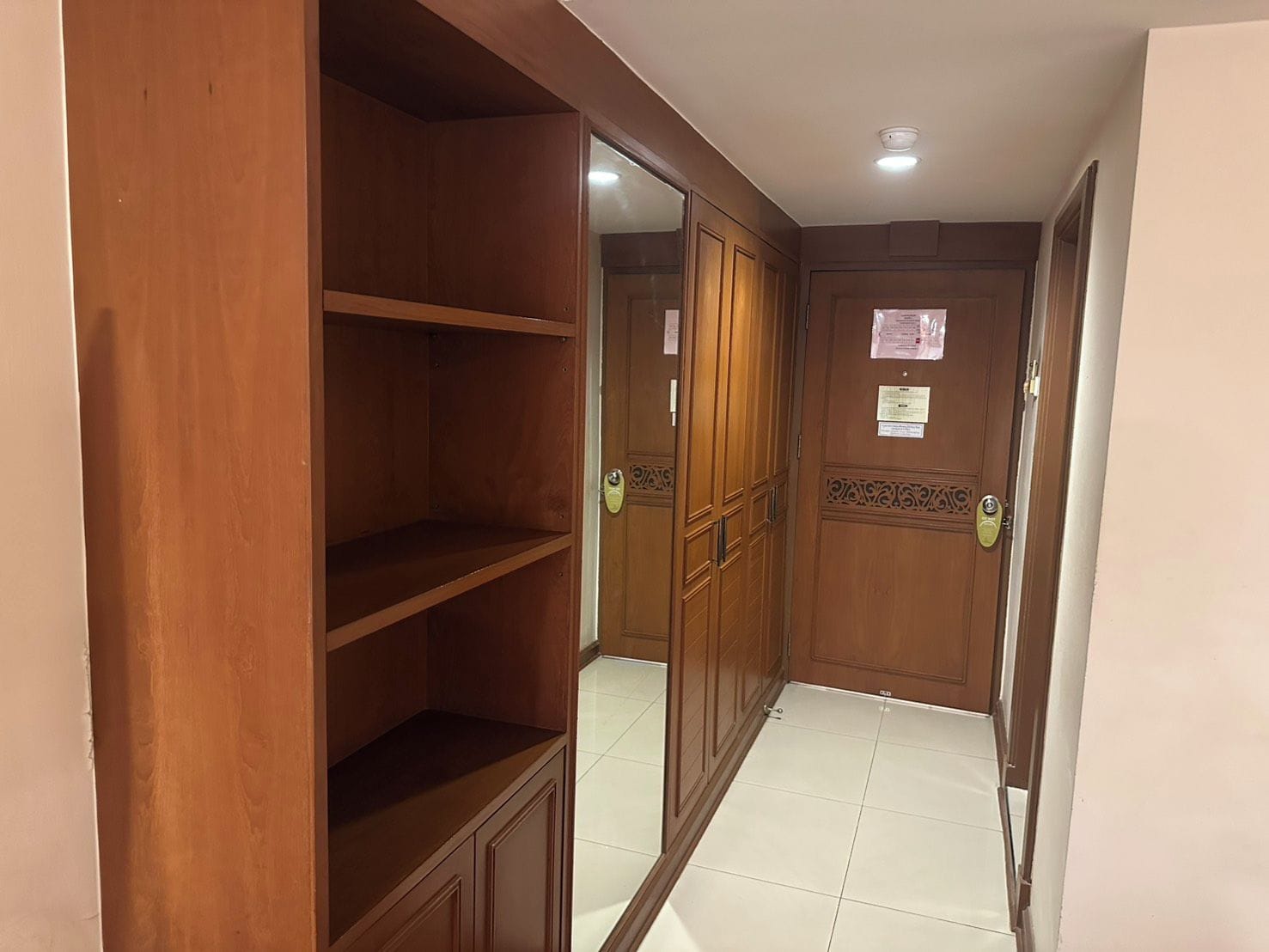 A hallway with wooden wardrobes and a tiled floor.