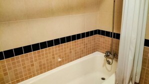 A standard bathtub with a showerhead, a drain, and a curtain.