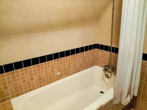 A standard bathtub with a showerhead, a drain, and a curtain.