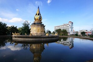 Una fuente con una escultura central, rodeada por un estanque reflectante, con un edificio de varios pisos al fondo.
