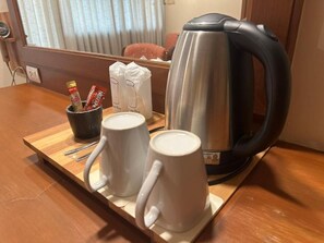 Una mesa de madera con dos tazas blancas, una tetera de acero inoxidable y una taza negra con asa.