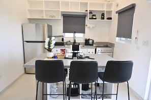 Une cuisine moderne dotée d’un îlot central, de chaises noires, d’un réfrigérateur et de divers appareils électroménagers.