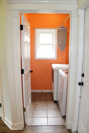 A narrow hallway with an orange wall, a window, and a laundry area with a washing machine.