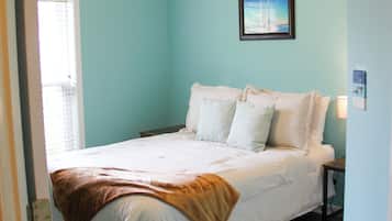 A bedroom with a bed, a ceiling fan, a window, and a wall-mounted picture.