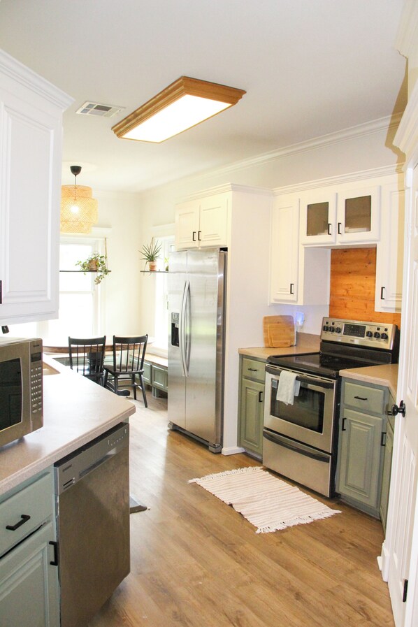 A kitchen with white cabinets, stainless steel appliances, a wooden countertop, and a dining area with a chair and table.