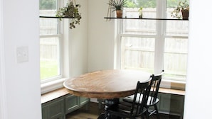A dining area with a round table, chairs, a hanging light fixture, and potted plants on shelves. - Aryn Ridge House / 3BR / Near Casinos & Interstate (Lake Charles)