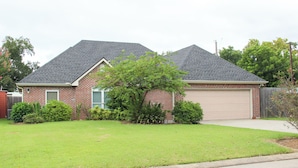 A two-story house with a garage, surrounded by a well-maintained lawn and various shrubs. - Aryn Ridge House / 3BR / Near Casinos & Interstate (Lake Charles)